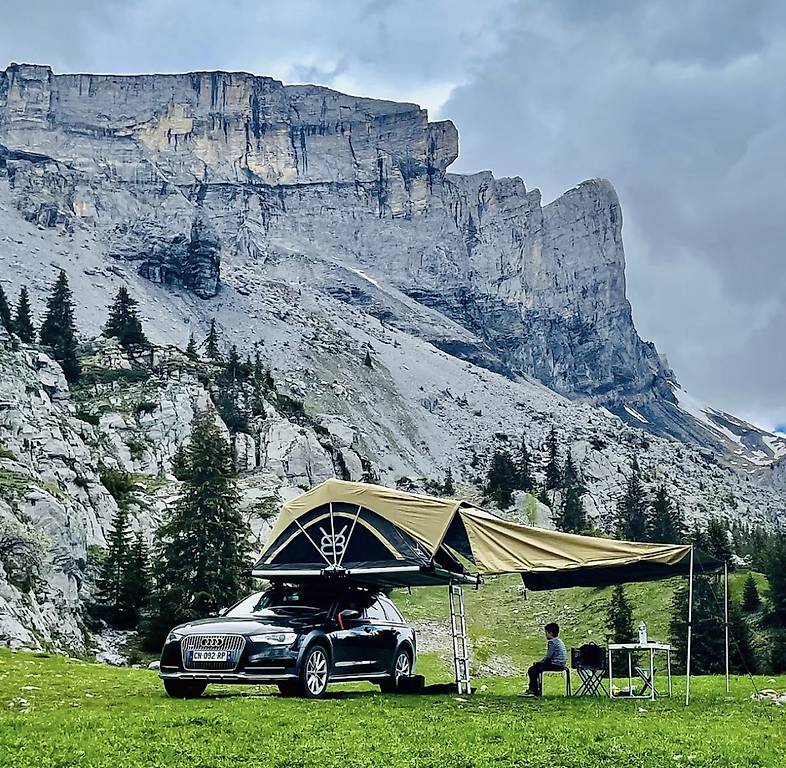 Un véhicule avec une tente de toit V8 ouverte, sous une falaise