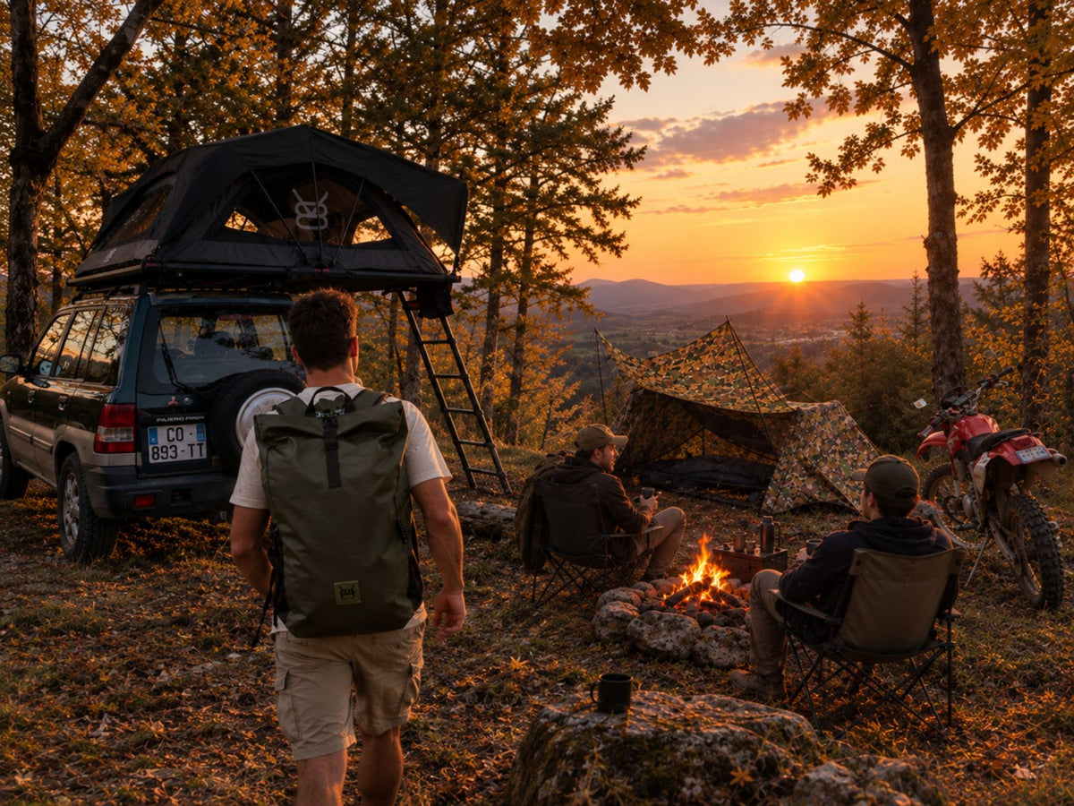 Un camp au coucher du soleil : la tente de toit ouverte sur le 4×4, un marcheur sac au dos, la tente moto montée près du feu.